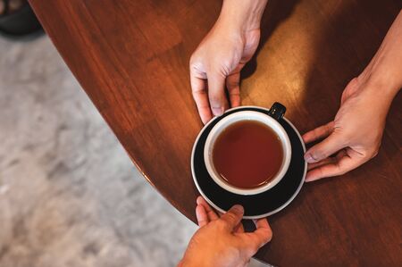 Close up of hands barista man serving coffee in coffee shop. male hands placing a cup of coffee on table. Coffee, Barista, extraction, serve, cafe, lifestyle concept.の写真素材