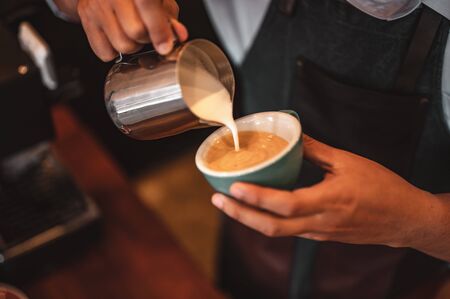 Close-up of professionally extracting coffee by barista with a pouring steamed milk into coffee cup making beautiful latte art. coffee, extraction, deep, cup, art, barista concept. の写真素材