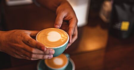 Close up of hands barista man serving coffee in coffee shop. male hands placing a cup of coffee on table. Coffee, Barista, extraction, serve, cafe, lifestyle concept.の写真素材