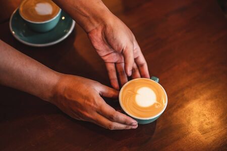 Close up of hands barista man serving coffee in coffee shop. male hands placing a cup of coffee on table. Coffee, Barista, extraction, serve, cafe, lifestyle concept.の写真素材