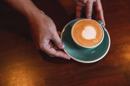 Close up of hands barista man serving coffee in coffee shop. male hands placing a cup of coffee on table. Coffee, Barista, extraction, serve, cafe, lifestyle concept.の写真素材