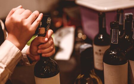The bartender opens a bottle of red wine using a wine opener. To pour a lot of empty glasses at the bar counter. Blurred background. wine, tasting, open, beverage, bartender, dinner concept.の写真素材