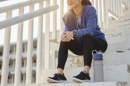 jogging, fitness, running, exercise, lifestyle, healthy concept. Young women warm up body. Sit back and Drink whey protein rest after running jogging on the running track around the football field.の写真素材