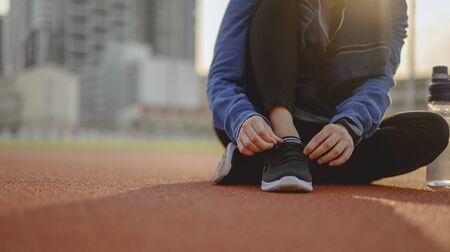 jogging, fitness, running, exercise, lifestyle, healthy concept. Young women using their hands to tie their shoes. warm up body running jogging on the running track around the football field.の写真素材