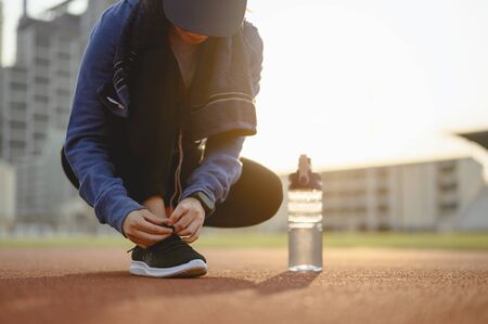 jogging, fitness, running, exercise, lifestyle, healthy concept. Young women using their hands to tie their shoes. warm up body running jogging on the running track around the football field.の写真素材