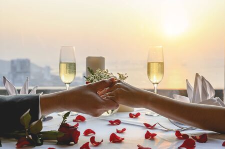 Couple holding hands having a dinner date at restaurant in sunset view. Valentine's, Couple, Honeymoon, Dinner, Wine, Romantic concept. の写真素材