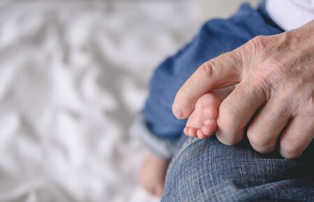The grandfather holding feet his newborn baby at home in holiday. Family, senior, grandson, baby, grandfather, Happy, lifestyle concept.の写真素材