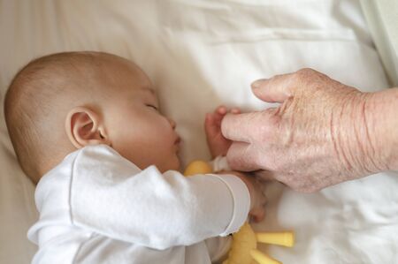 The grandfather holding hand while his newborn baby sleeping at home in holiday. Family, senior, grandson, baby, grandfather, Happy, lifestyle concept.の写真素材