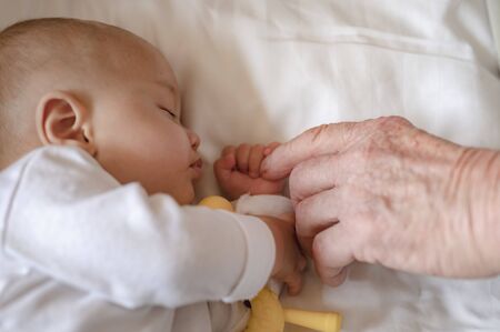 The grandfather holding hand while his newborn baby sleeping at home in holiday. Family, senior, grandson, baby, grandfather, Happy, lifestyle concept.の写真素材