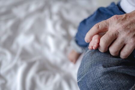 The grandfather holding feet his newborn baby at home in holiday. Family, senior, grandson, baby, grandfather, Happy, lifestyle concept.の写真素材