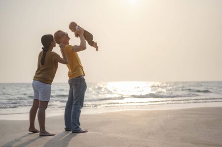 Father is carrying and playing with toddler baby son and mother having fun at the beach on sunset in holiday. Family, beach, relax, son, baby, lifestyle concept.の写真素材