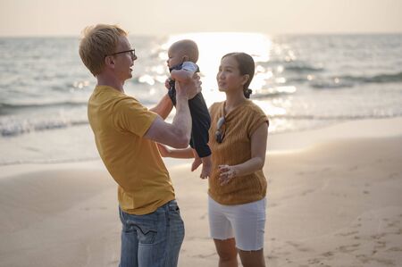 Father is carrying and playing  toddler baby son and mother having fun at the beach on sunset in...