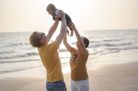 Father is carrying and playing with toddler baby son and mother having fun at the beach on sunset in holiday. Family, beach, relax, son, baby, lifestyle concept.の写真素材