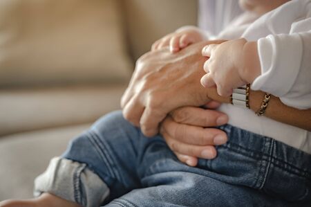 The mother's hand that holds the child on the sofa at home. Family, mother, son, baby, Happy, lifestyle concept.の写真素材
