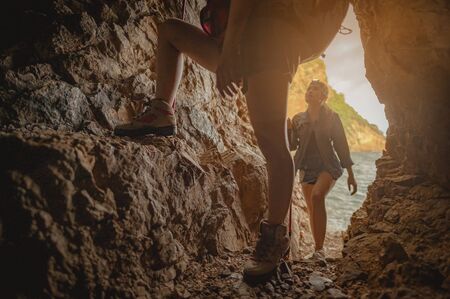 Side view  woman hiker climbing on the cliff at cave in sunset.の写真素材