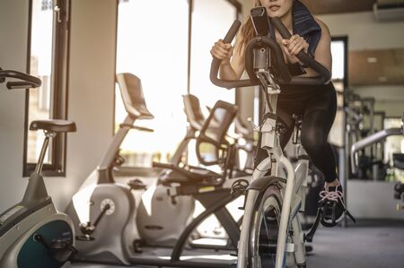 Front view of woman workout with bike. Women exercise working out in the gym for healthy lifestyle on bike at sunset. fitness ,workout, gym exercise ,lifestyle  and healthy concept.の写真素材
