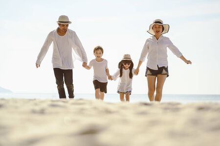 Parents are holding hands their children and walking on the beach at sunset in holiday.の写真素材