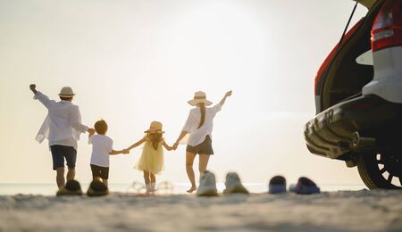 Family, travel, beach, relax, lifestyle, holiday concept. Family who enjoy a picnic. Parents are holding hands their children and walking on the beach at sunset in holiday. の写真素材