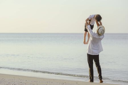 Family, travel, beach, relax, lifestyle, holiday concept. Family who enjoy a picnic. Father is carrying his son at the beach on sunset in holiday. の写真素材