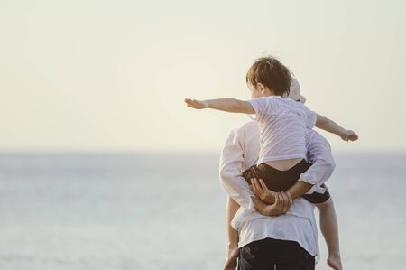 Family, travel, beach, relax, lifestyle, holiday concept. Family who enjoy a picnic. Father is carrying his son at the beach on sunset in holiday. の写真素材