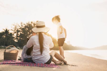 Family, travel, beach, relax, lifestyle, holiday concept. Parents and children who enjoy a picnic at the beach on sunset in holiday. の写真素材