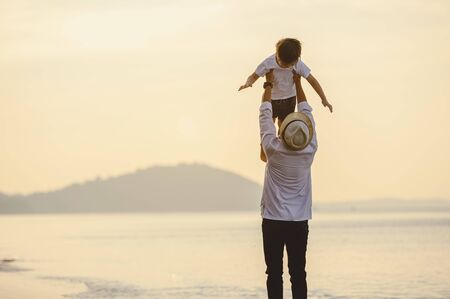 Family, travel, beach, relax, lifestyle, holiday concept. Family who enjoy a picnic. Father is carrying his son at the beach on sunset in holiday. の写真素材