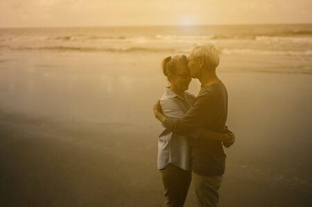 Senior lovers happily hug and kiss each other around the beach at sunset and soak up the atmosphere.の写真素材