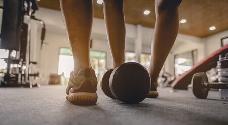 fitness, jogging, running, exercise, lifestyle and healthy concept. Close-up the back of the young man's legs wear sportswear, prepare dumbbell weights for exercise in the gym at sunset.の写真素材