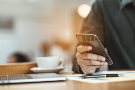 A young employee is looking for business information using a mobile phone on a wooden table to plan a new project for the boss at the office. Problems and concepts for solving problemsの写真素材