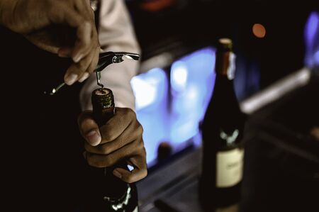The bartender opens a bottle of red wine using a wine opener. To pour a lot of empty glasses at the bar counter. The background is blurred.の写真素材