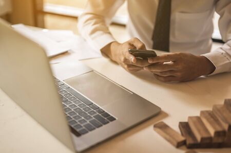 A young employee is looking for business information using a mobile phone on a wooden table to plan a new project for the boss at the office. Problems and concepts for solving problemsの写真素材