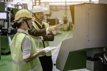 Male and female industrial engineers wearing helmets are using laptops to study and talk about new projects in industrial plants. They acted happily and professionally. Engineering and architecture technology for factory industry concept.の写真素材