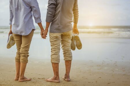 Senior couple standing on the beach holding hands at sunset, plan life insurance at retirement concept.の写真素材