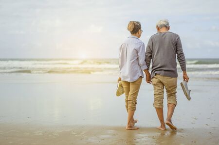 Senior couple walking on the beach holding hands at sunrise, plan life insurance at retirement concept.の写真素材