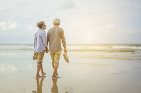 Senior couple walking on the beach holding hands at sunrise, plan life insurance at retirement concept.の写真素材