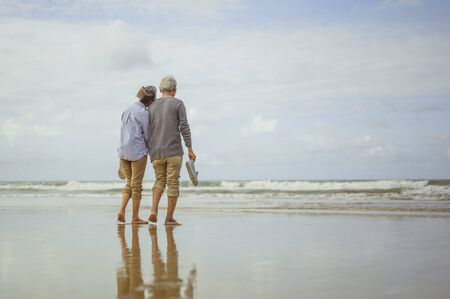 Senior couple walking on the beach holding hands at sunrise, plan life insurance at retirement concept.の写真素材