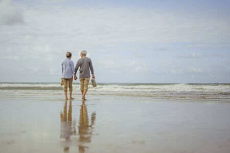 Senior couple walking on the beach holding hands at sunrise, plan life insurance at retirement concept.の写真素材