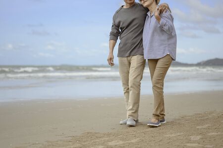 Senior lovers walk hand in hand at the beach at sunrise, plan life insurance at retirement concept.の写真素材