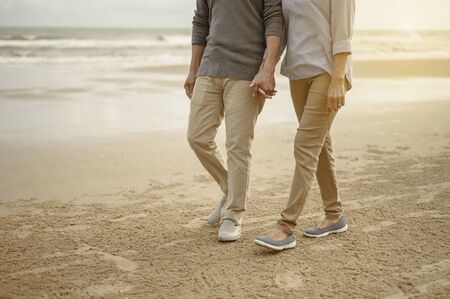 Senior lovers walk hand in hand at the beach at sunset, plan life insurance at retirement concept.の写真素材