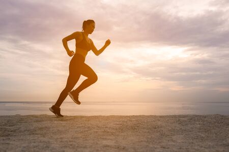silhouette of  runner woman in running workout training at sunset beach.Silhouette of an athletic woman running on the beach during sunset time.の写真素材
