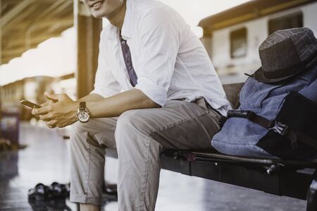 Man sitting with mobile phone and bag waiting for train.Work and travel concept.の写真素材