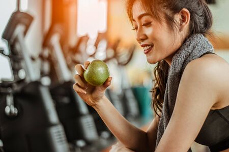 Athletic woman resting after working out in the gym.sitting on a treadmill and eating an apple.の写真素材