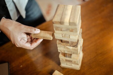 business man hand  pulling out or placing wood block on the tower in modern office. plan and strategy in business. blur for background.の写真素材