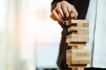 business man hand  pulling out or placing wood block on the tower in modern office. plan and strategy in business. blur for background.の写真素材