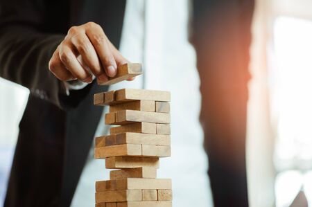 business man hand  pulling out or placing wood block on the tower in modern office. plan and strategy in business. blur for background.の写真素材