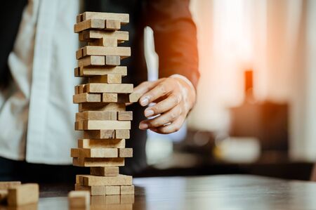 business man hand  pulling out or placing wood block on the tower in modern office. plan and strategy in business. blur for background.の写真素材