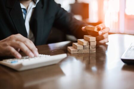 plan and strategy in business.risk concept.hand of man has piling up and stacking a wooden block.Businessman Building The Success.using calculator to calculate.の写真素材