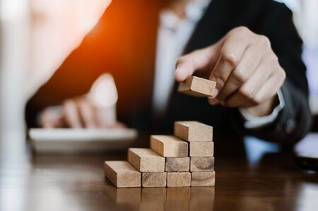 plan and strategy in business.risk concept.hand of man has piling up and stacking a wooden block.Businessman Building The Success.using calculator to calculate.の写真素材