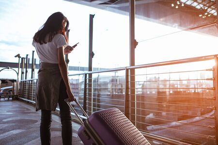 Young woman pulling suitcase in modern airport terminal. Travelling guy with his luggage while waiting for transport. Rear view. Copy spaceの写真素材