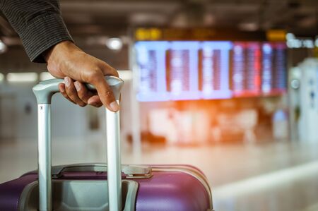 close up man hand touching baggage for check in at flight timetable in international airport.の写真素材